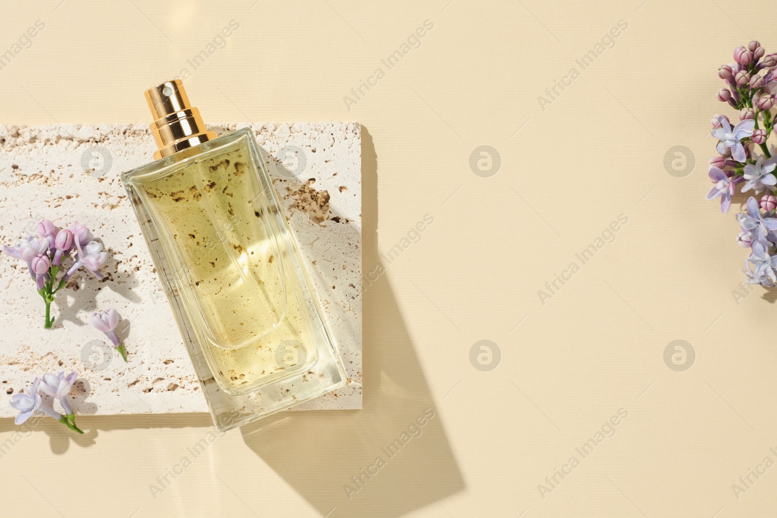 Bottle of perfume and beautiful lilac flowers on pale yellow background, flat lay. Space for text Photo of Bottle of perfume and beautiful lilac flowers on pale yellow background, flat lay. Space for text