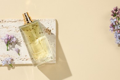 Photo of Bottle of perfume and beautiful lilac flowers on pale yellow background, flat lay. Space for text