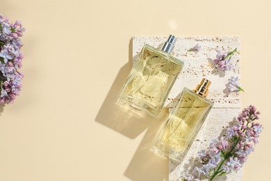 Photo of Luxury perfumes and beautiful lilac flowers on pale yellow background, flat lay. Space for text