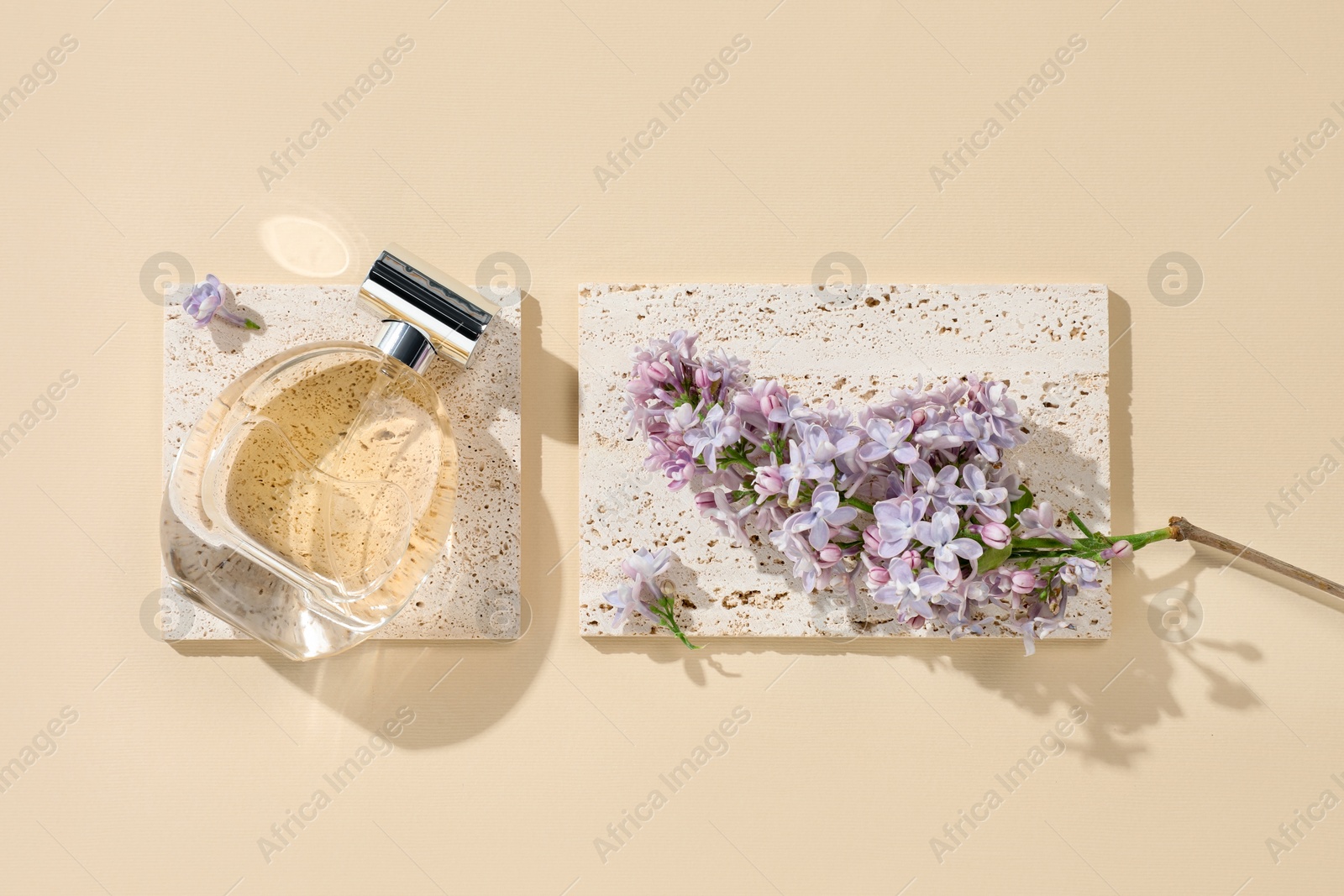 Bottle of perfume and beautiful lilac flowers on pale yellow background, flat lay Photo of Bottle of perfume and beautiful lilac flowers on pale yellow background, flat lay