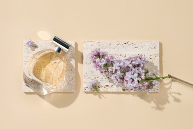 Photo of Bottle of perfume and beautiful lilac flowers on pale yellow background, flat lay