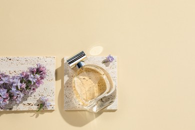 Photo of Bottle of perfume and beautiful lilac flowers on pale yellow background, flat lay. Space for text
