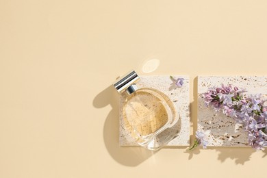 Photo of Bottle of perfume and beautiful lilac flowers on pale yellow background, flat lay. Space for text