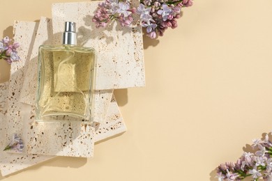 Photo of Bottle of perfume and beautiful lilac flowers on pale yellow background, flat lay. Space for text
