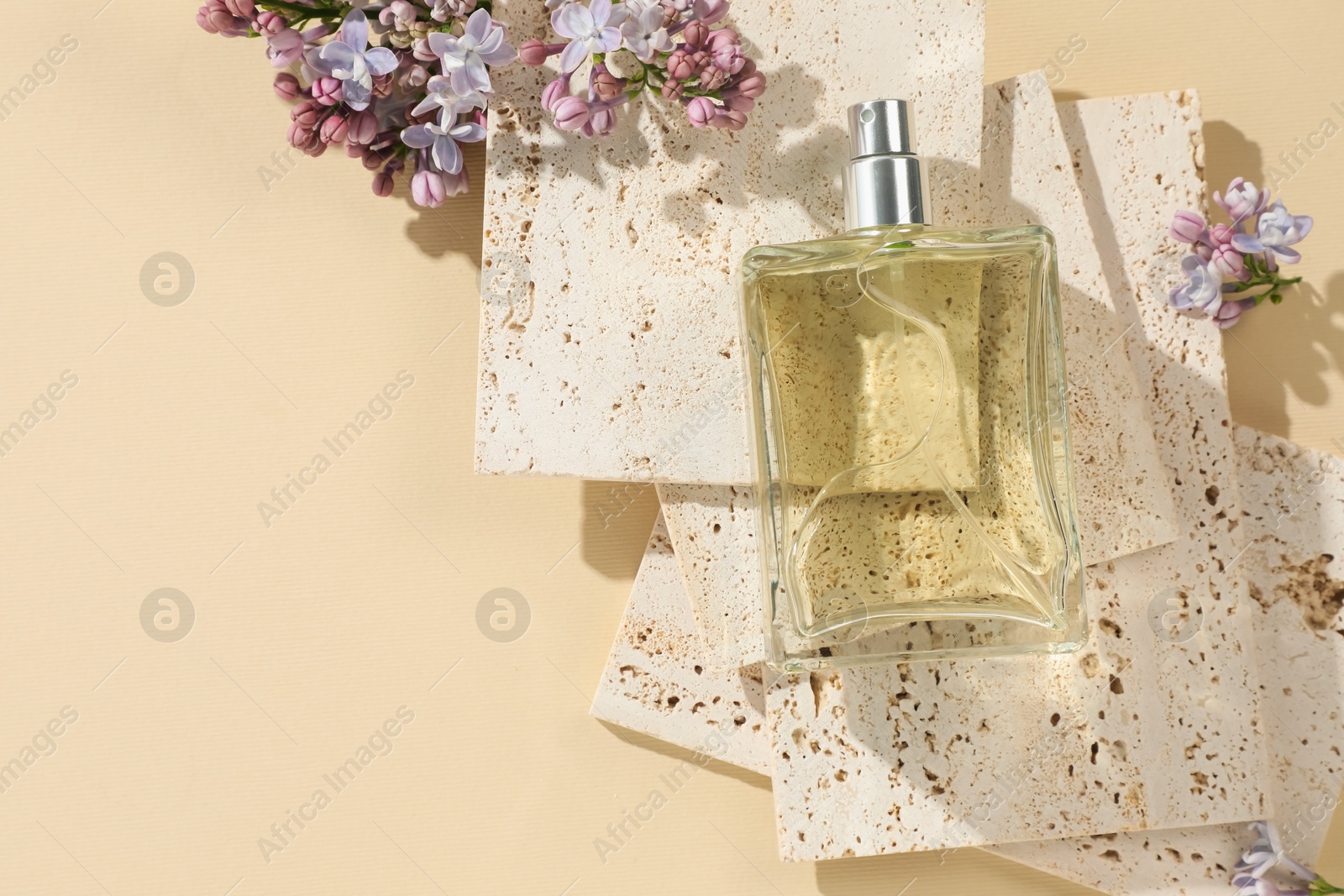 Bottle of perfume and beautiful lilac flowers on pale yellow background, flat lay. Space for text Photo of Bottle of perfume and beautiful lilac flowers on pale yellow background, flat lay. Space for text