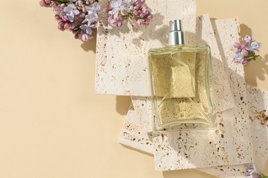 Photo of Bottle of perfume and beautiful lilac flowers on pale yellow background, flat lay. Space for text