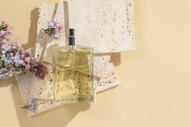 Photo of Bottle of perfume and beautiful lilac flowers on pale yellow background, flat lay. Space for text