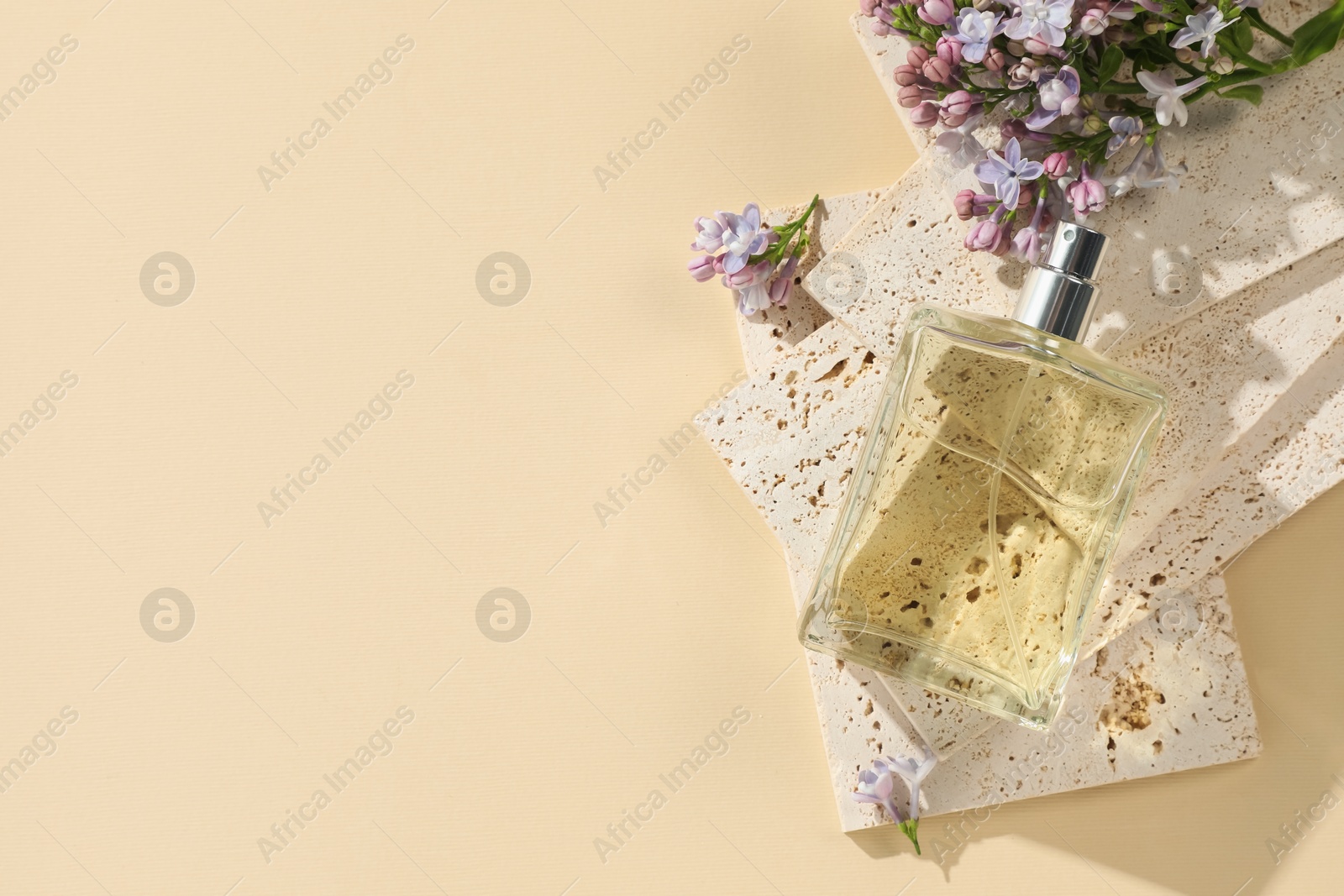 Bottle of perfume and beautiful lilac flowers on pale yellow background, flat lay. Space for text Photo of Bottle of perfume and beautiful lilac flowers on pale yellow background, flat lay. Space for text