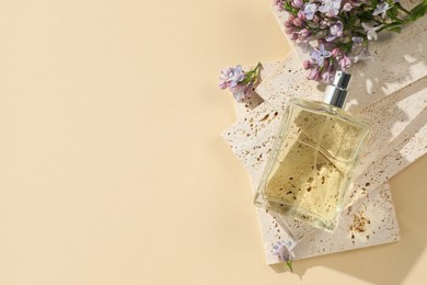 Photo of Bottle of perfume and beautiful lilac flowers on pale yellow background, flat lay. Space for text