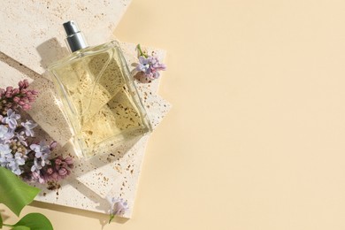 Photo of Bottle of perfume and beautiful lilac flowers on pale yellow background, flat lay. Space for text