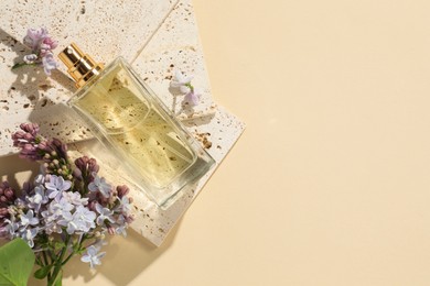 Photo of Bottle of perfume and beautiful lilac flowers on pale yellow background, flat lay. Space for text