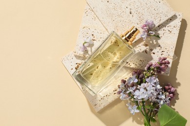 Photo of Bottle of perfume and beautiful lilac flowers on pale yellow background, flat lay. Space for text