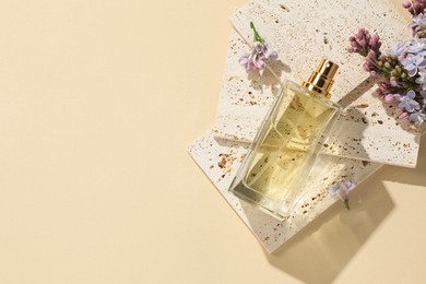 Photo of Bottle of perfume and beautiful lilac flowers on pale yellow background, flat lay. Space for text