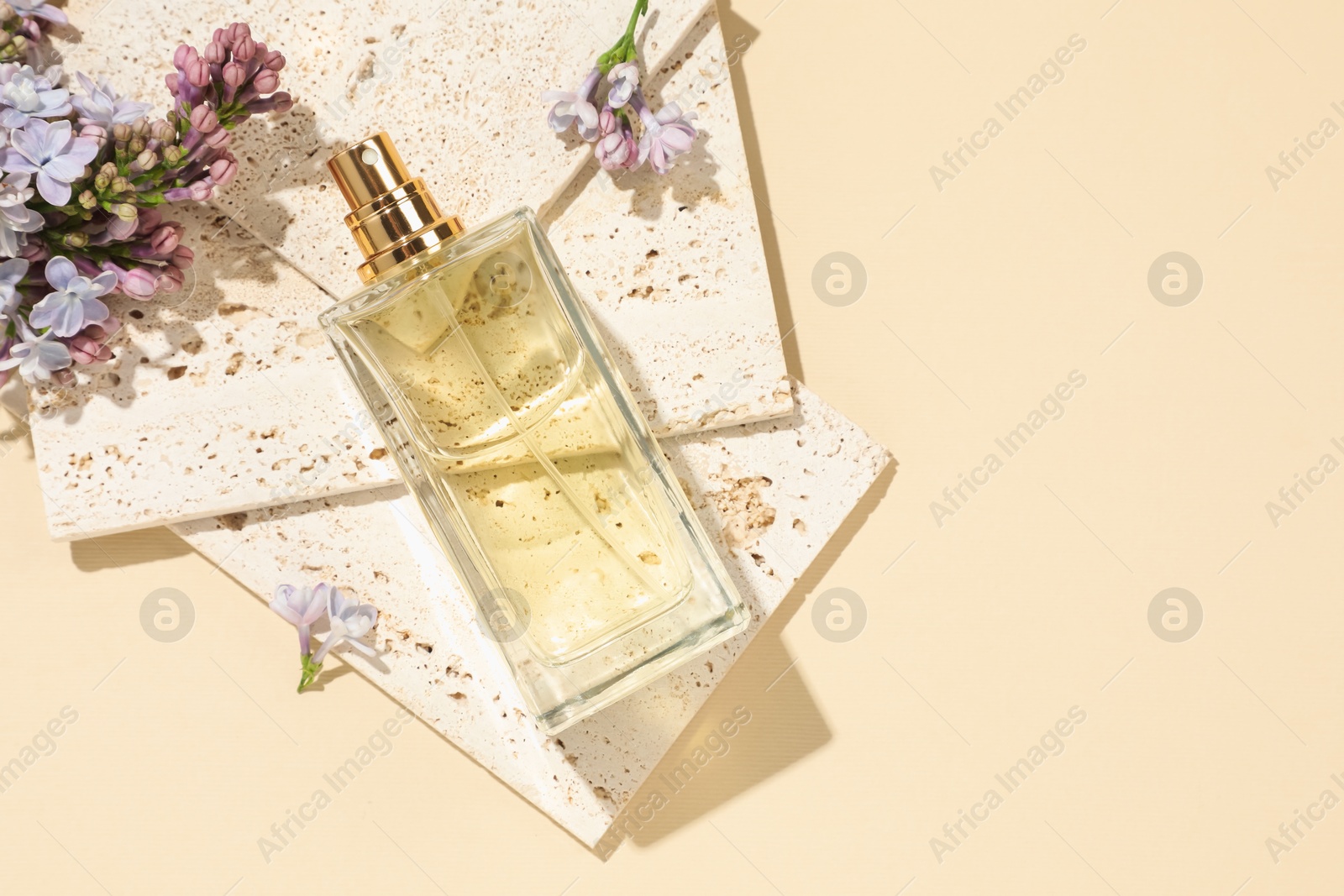Bottle of perfume and beautiful lilac flowers on pale yellow background, flat lay. Space for text Photo of Bottle of perfume and beautiful lilac flowers on pale yellow background, flat lay. Space for text