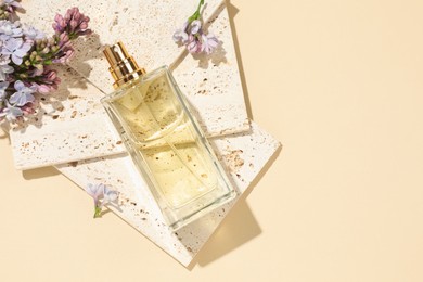 Photo of Bottle of perfume and beautiful lilac flowers on pale yellow background, flat lay. Space for text