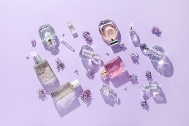 Photo of Luxury perfumes and beautiful lilac flowers on light violet background, flat lay