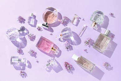Photo of Luxury perfumes and beautiful lilac flowers on light violet background, flat lay