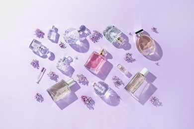 Photo of Luxury perfumes and beautiful lilac flowers on light violet background, flat lay