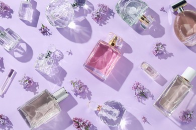 Photo of Luxury perfumes and beautiful lilac flowers on light violet background, flat lay