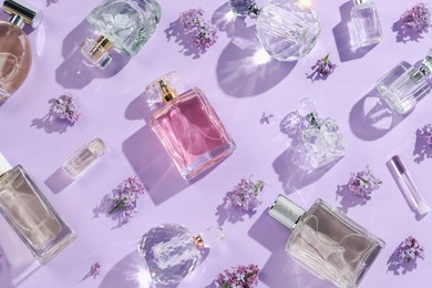 Photo of Luxury perfumes and beautiful lilac flowers on light violet background, flat lay