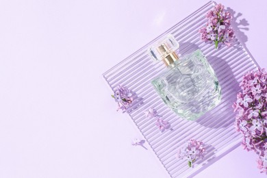 Photo of Bottle of perfume and beautiful lilac flowers on light violet background, flat lay. Space for text