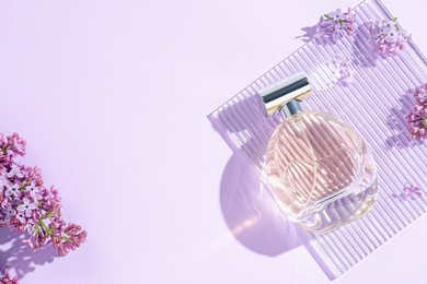 Photo of Bottle of perfume and beautiful lilac flowers on light violet background, flat lay. Space for text