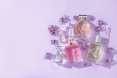 Photo of Luxury perfumes and beautiful lilac flowers on light violet background, flat lay. Space for text