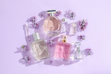 Photo of Luxury perfumes and beautiful lilac flowers on light violet background, flat lay