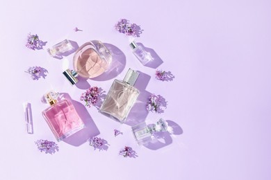 Photo of Luxury perfumes and beautiful lilac flowers on light violet background, flat lay. Space for text