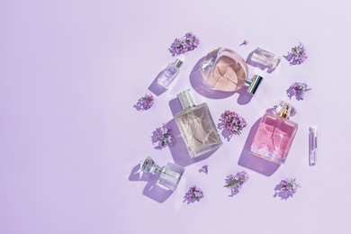 Photo of Luxury perfumes and beautiful lilac flowers on light violet background, flat lay. Space for text