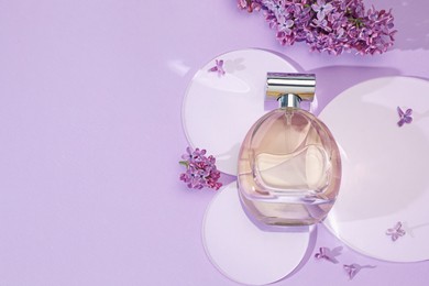 Photo of Bottle of perfume and beautiful lilac flowers on light violet background, flat lay. Space for text