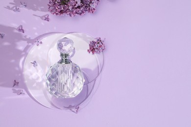 Photo of Bottle of perfume and beautiful lilac flowers on light violet background, flat lay. Space for text