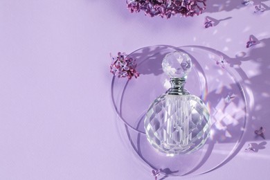 Photo of Bottle of perfume and beautiful lilac flowers on light violet background, flat lay. Space for text