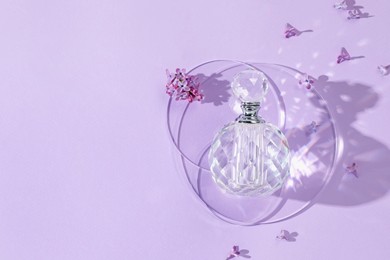 Photo of Bottle of perfume and beautiful lilac flowers on light violet background, flat lay. Space for text