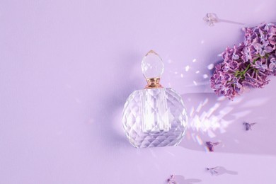 Photo of Bottle of perfume and beautiful lilac flowers on light violet background, flat lay. Space for text