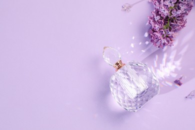 Photo of Bottle of perfume and beautiful lilac flowers on light violet background, flat lay. Space for text
