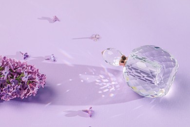 Photo of Bottle of perfume and beautiful lilac flowers on light violet background
