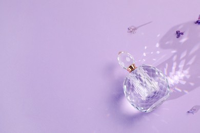 Photo of Bottle of perfume and beautiful lilac flowers on light violet background, flat lay. Space for text
