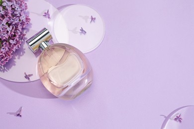 Photo of Bottle of perfume and beautiful lilac flowers on light violet background, flat lay. Space for text