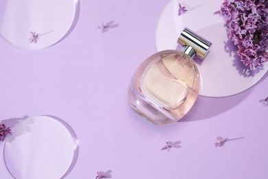 Photo of Bottle of perfume and beautiful lilac flowers on light violet background, flat lay