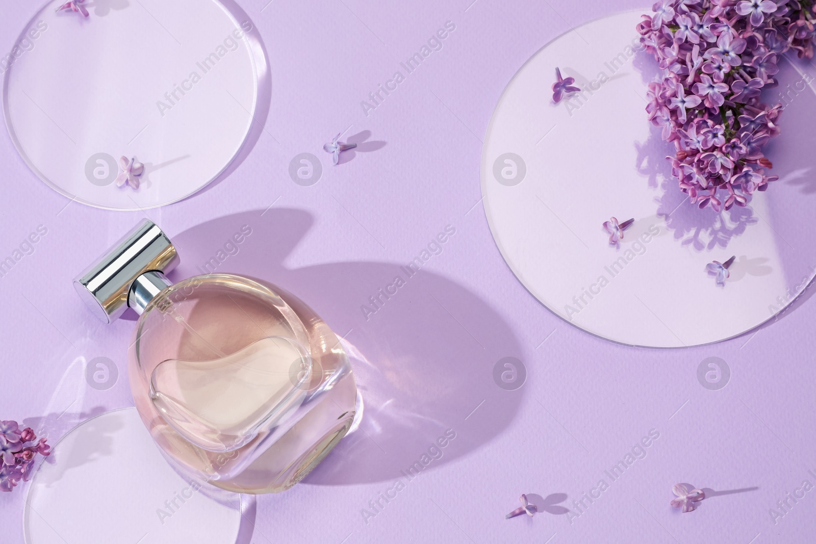 Bottle of perfume and beautiful lilac flowers on light violet background, flat lay Photo of Bottle of perfume and beautiful lilac flowers on light violet background, flat lay
