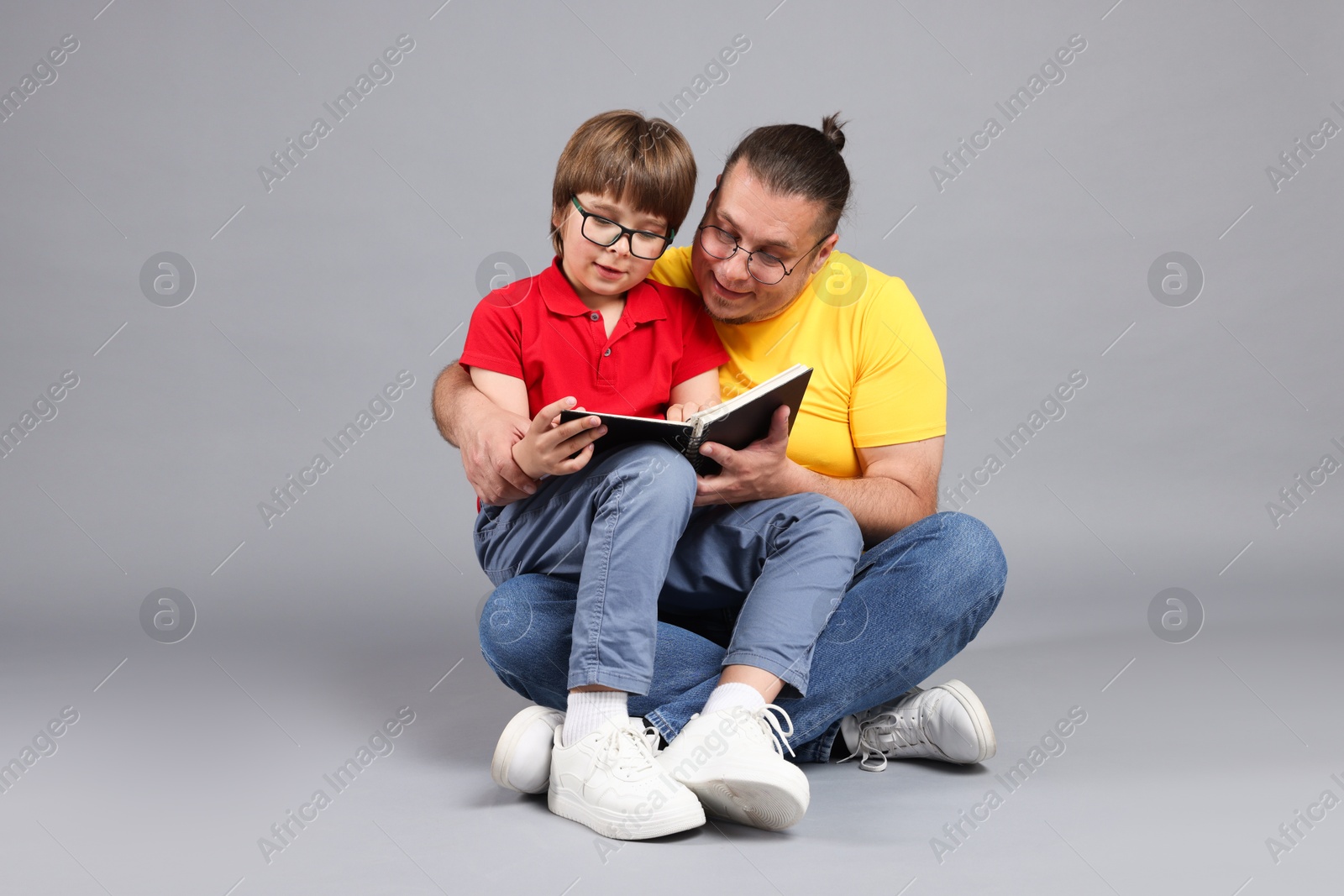 Father and his son reading book together on grey background Photo of Father and his son reading book together on grey background