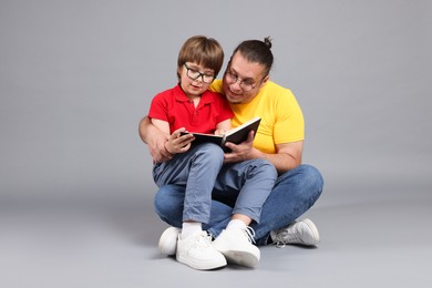 Photo of Father and his son reading book together on grey background
