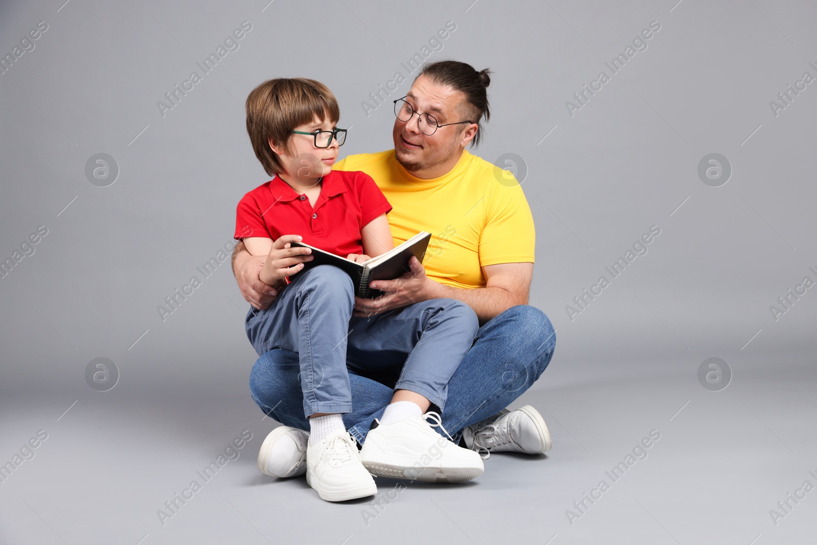 Father and his son reading book together on grey background Photo of Father and his son reading book together on grey background