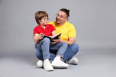 Photo of Father and his son reading book together on grey background