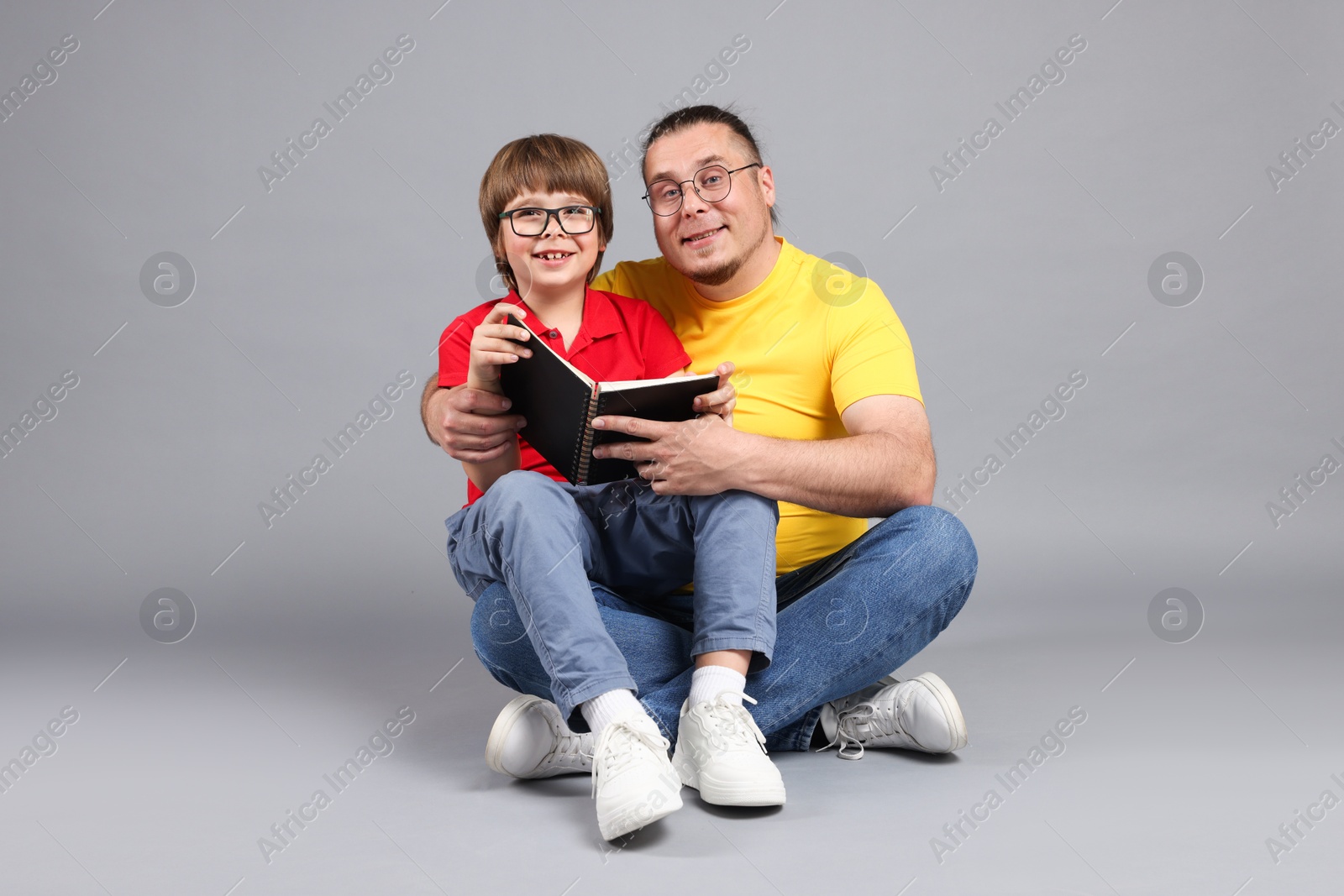 Father and his son reading book together on grey background Photo of Father and his son reading book together on grey background