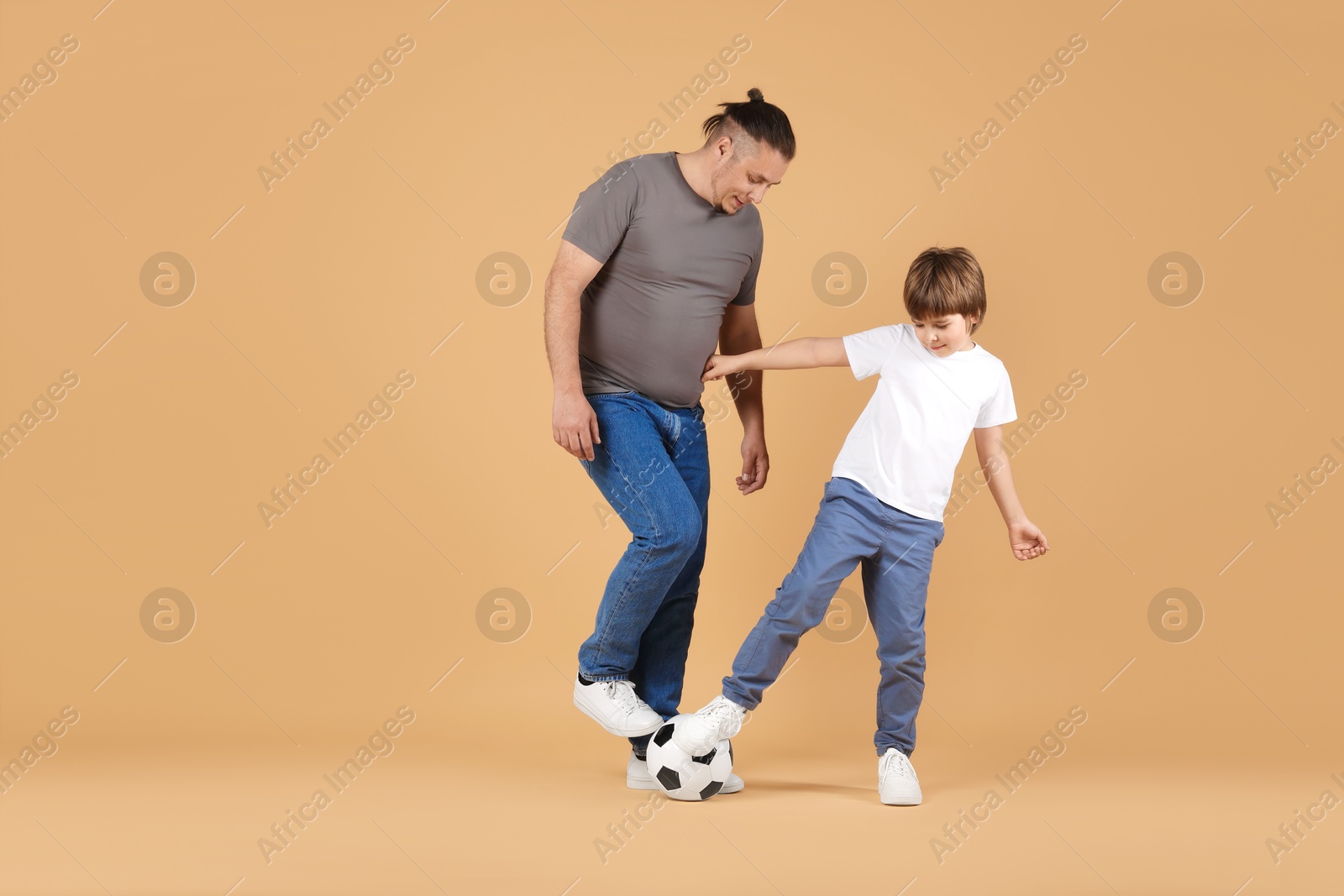Father and his son playing football on beige background Photo of Father and his son playing football on beige background