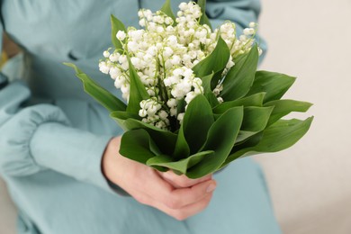 Photo of Woman with beautiful lilies of the valley flowers on sofa indoors, closeup