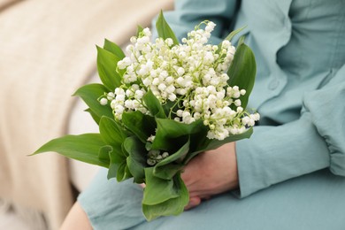 Photo of Woman with beautiful lilies of the valley flowers on sofa indoors, closeup