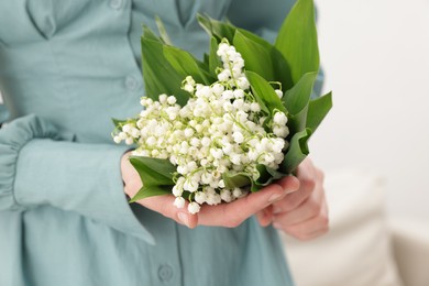Photo of Woman with beautiful lilies of the valley flowers indoors, closeup